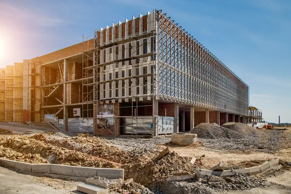 Multi-storey building under construction with cranes and cleared ground.