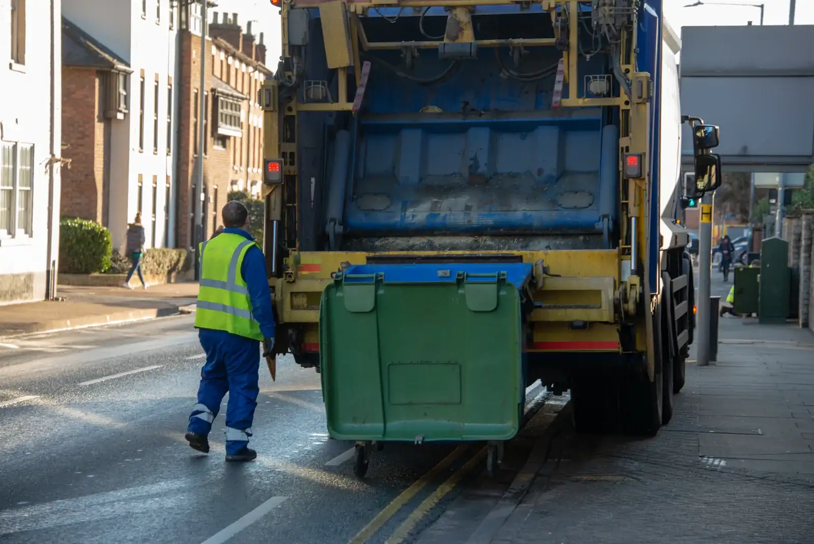A refuse collection worker moving a large wheeled bin to a collection vehicle.