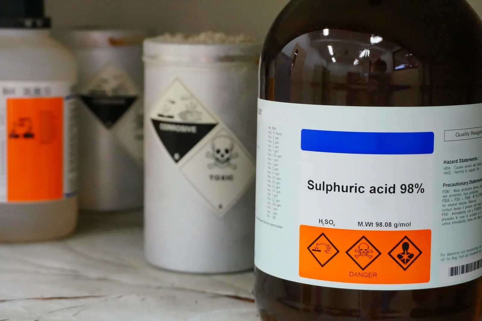 A labelled sulphuric-acid bottle with chemical hazard warnings.