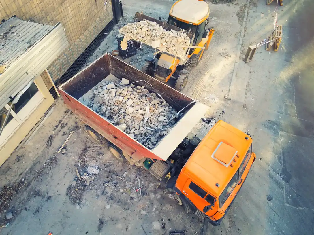 Loader tipping construction waste and debris into a dumper.