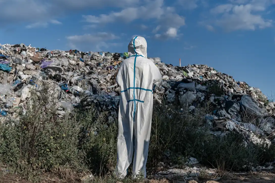 Worker in protective coveralls facing a waste pile.