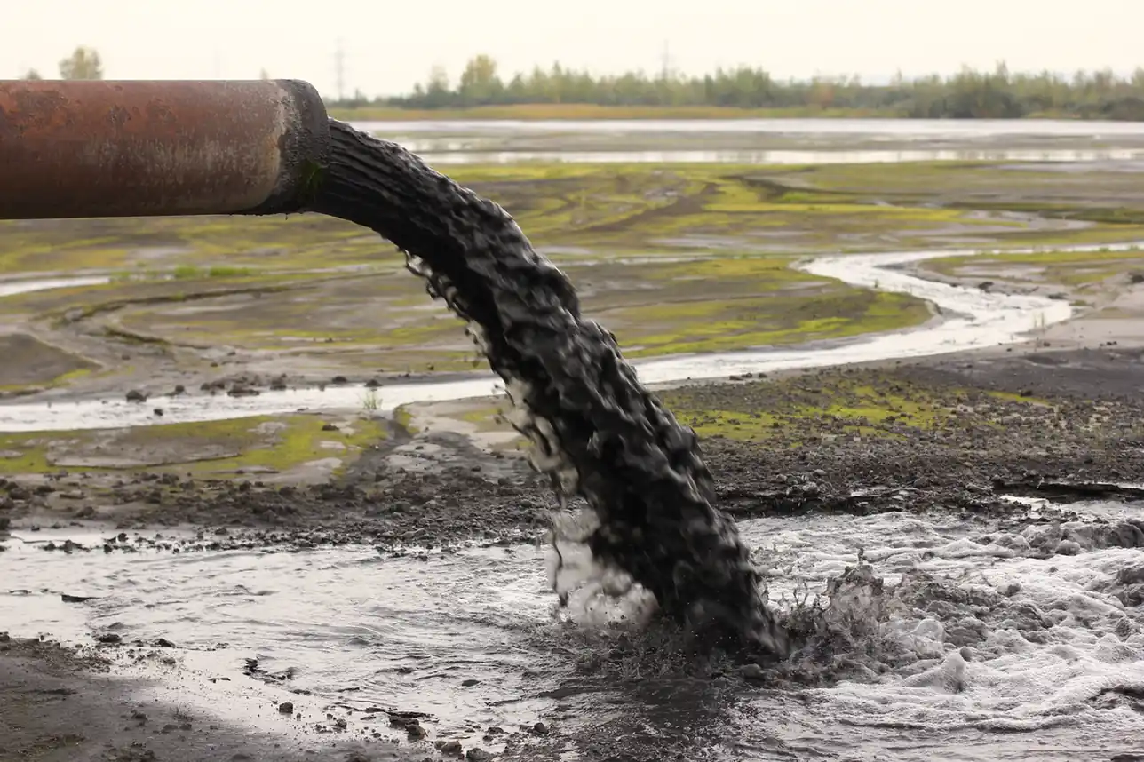 Industrial pipe discharging dark liquid waste onto open ground.