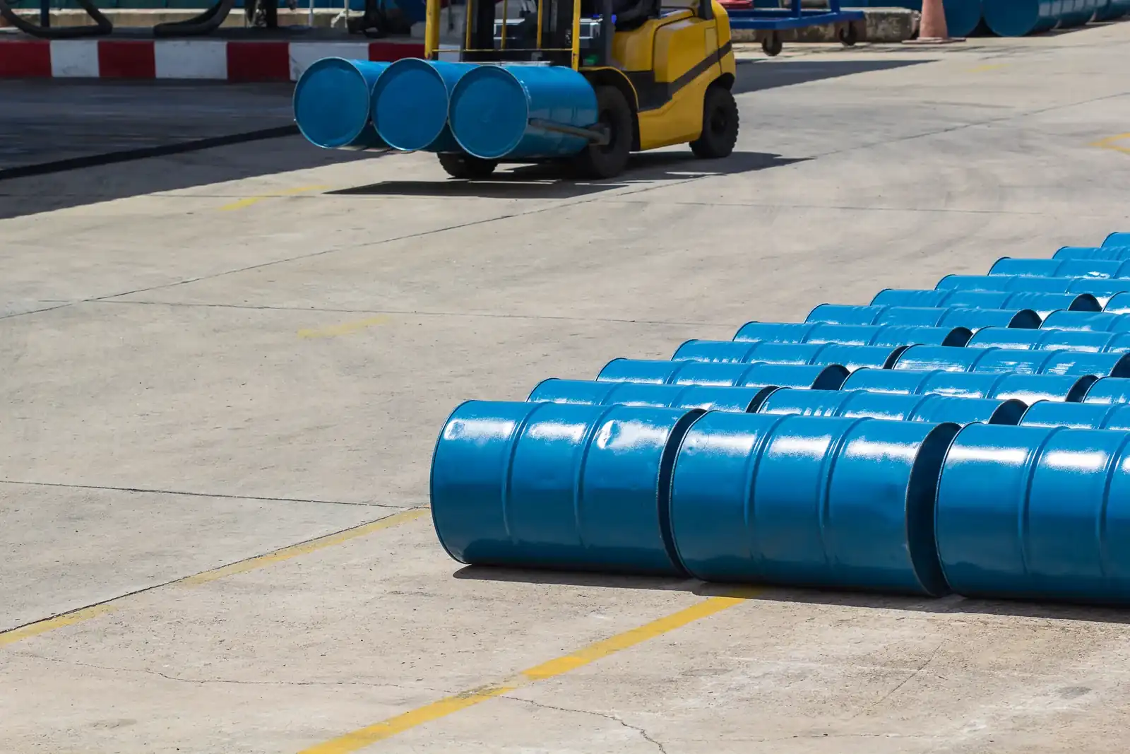 A forklift handling blue industrial drums in a storage yard.