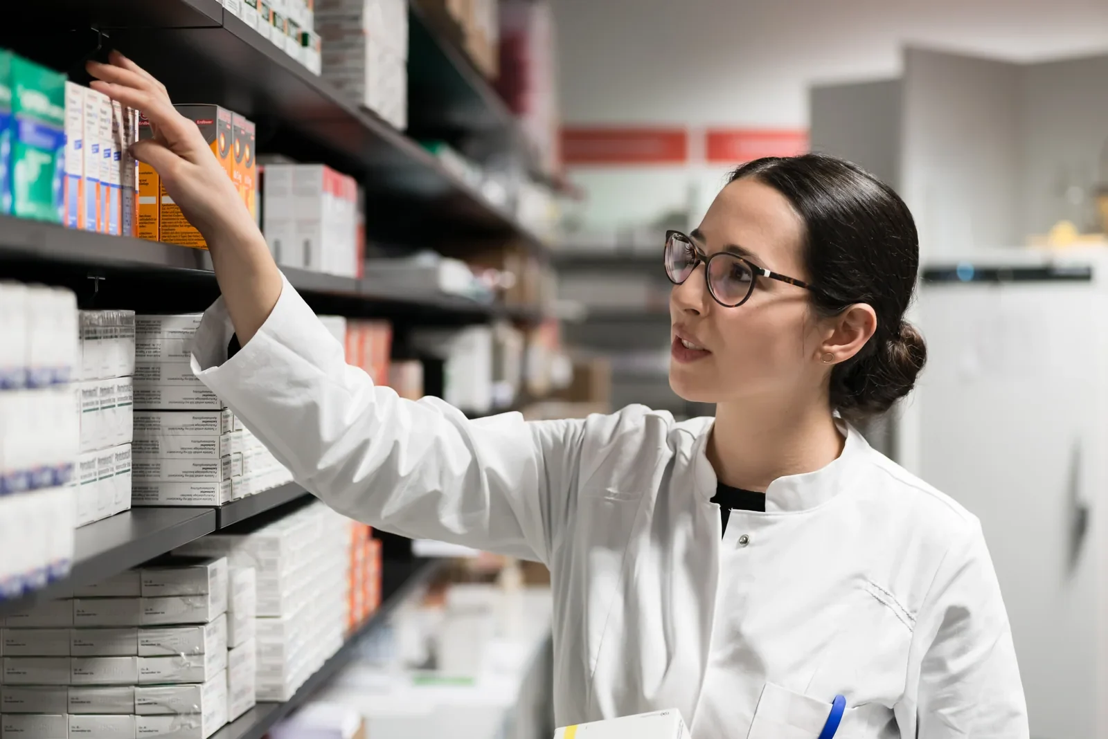 Pharmacist checking packaged medicines on pharmacy shelving.