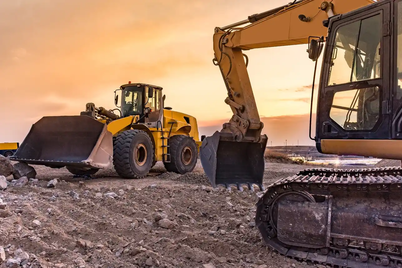 Wheel loader and excavator on a construction site at sunset.