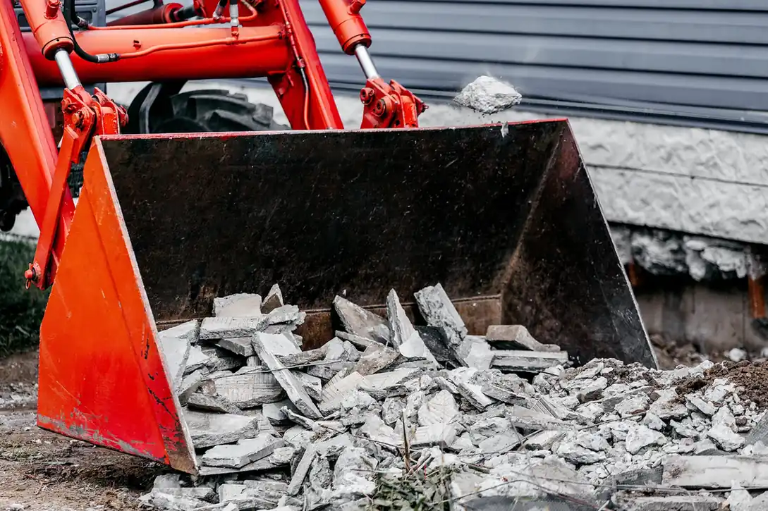 Loader bucket filled with broken concrete and paving slabs.