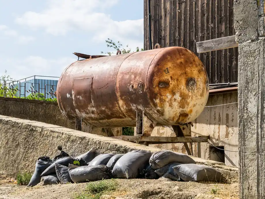 Old rusted metal storage tank outside a building.