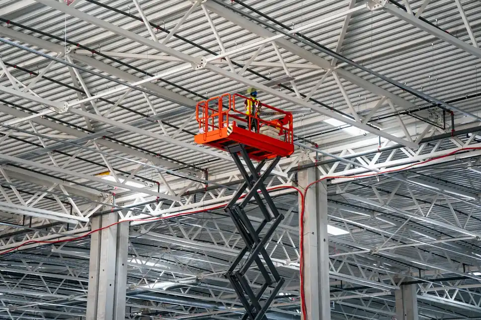 Scissor lift providing access to overhead steelwork inside an industrial building.