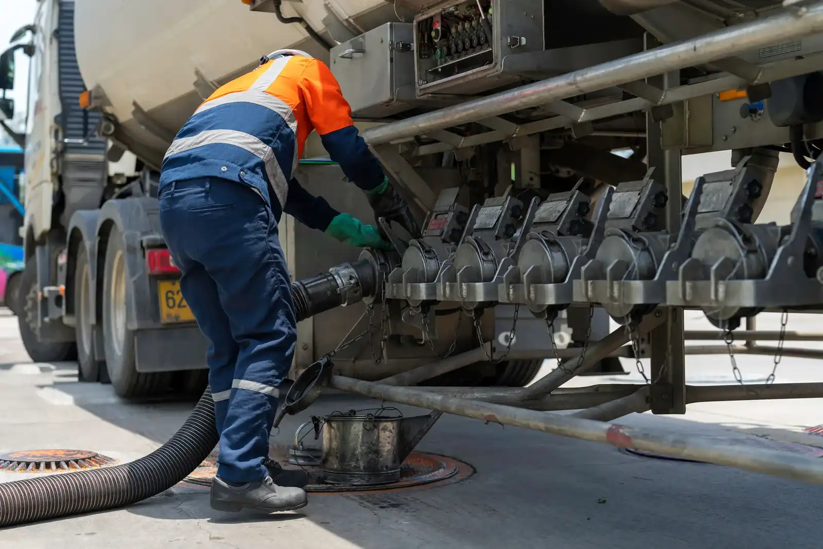 Operator handling a fuel delivery hose beside a road tanker.