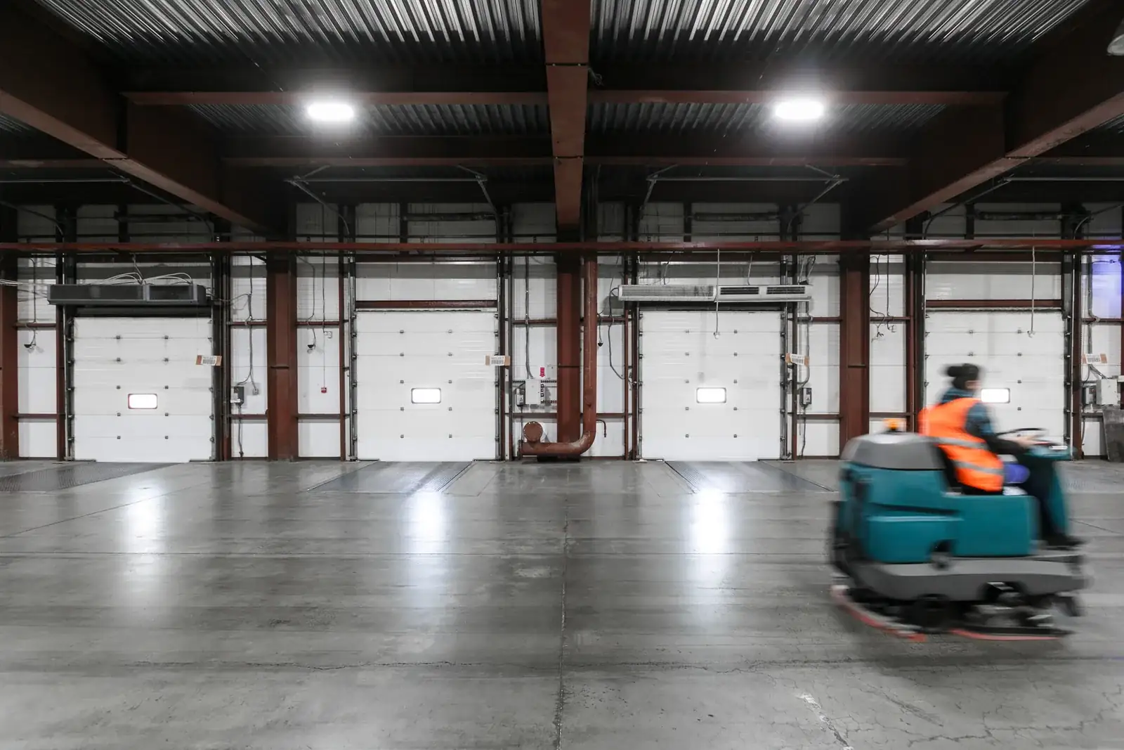 Operator driving a floor cleaning machine through a warehouse.