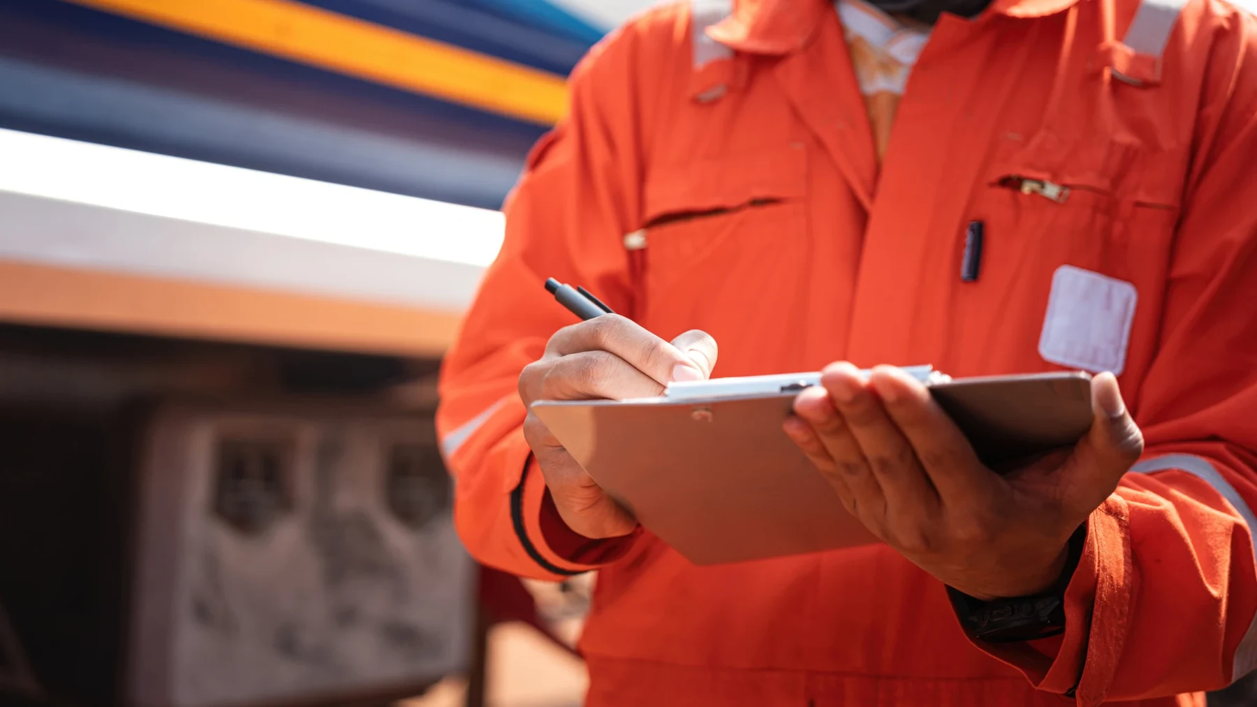 Engineer in orange overalls completing a checklist on a clipboard.
