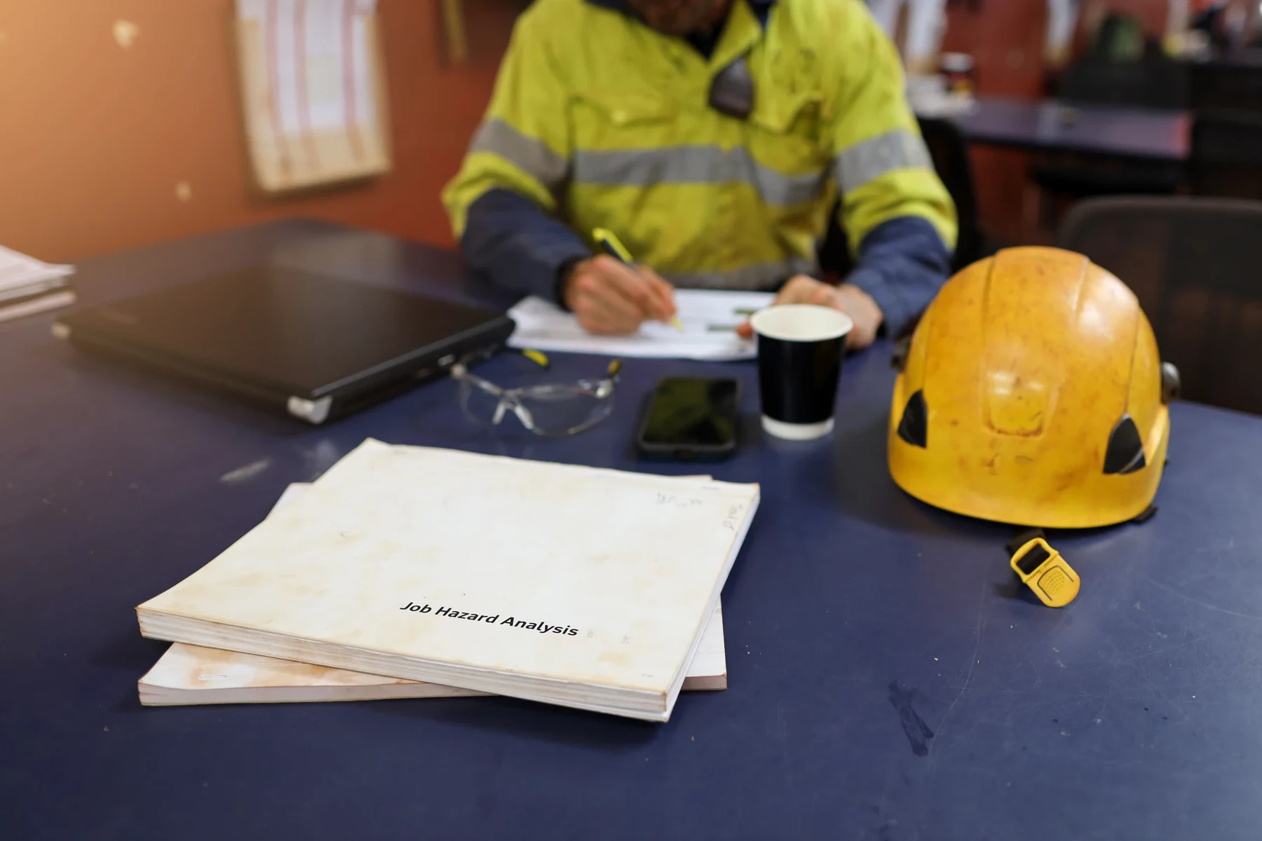 Job hazard analysis documents and a hard hat on a site office table.
