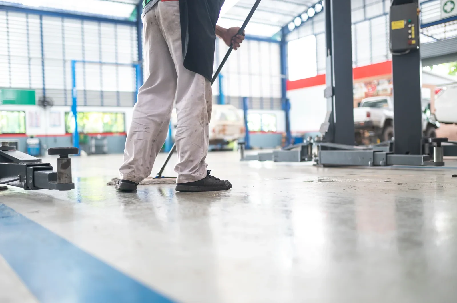 Worker using a floor squeegee in a vehicle repair workshop.